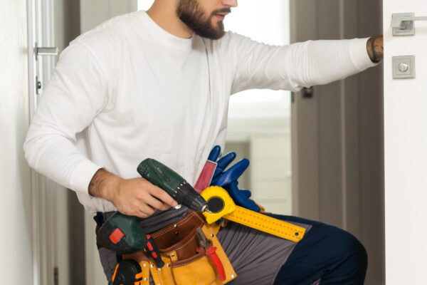 Handyman Fitting A New Door Using A Screwdriver At Home.