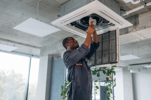 High up, fixing the ventilation. Repairman is indoors in the modern office.